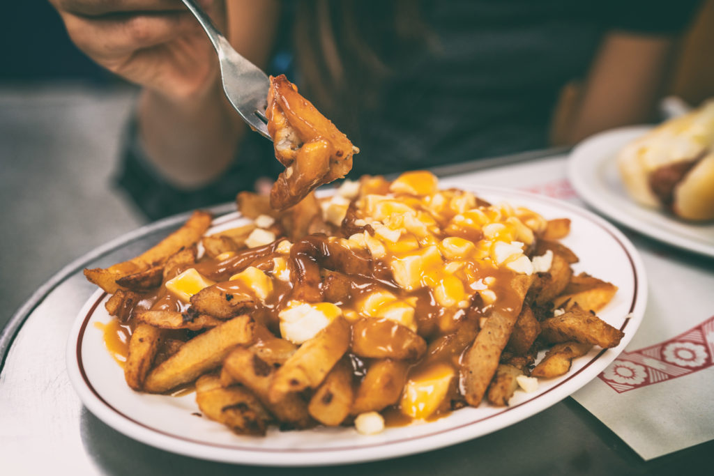 Poutine recipe french fries canadian local classic dish in the province of Quebec, Canada. Fast food retro diner restaurant serving plate of fried potates with brown gravy sauce and fresh cheese curds.