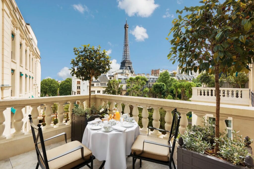 A pillared balcony with a table and chairs set up, overlooking the Eiffel Tower. Luxury hotels