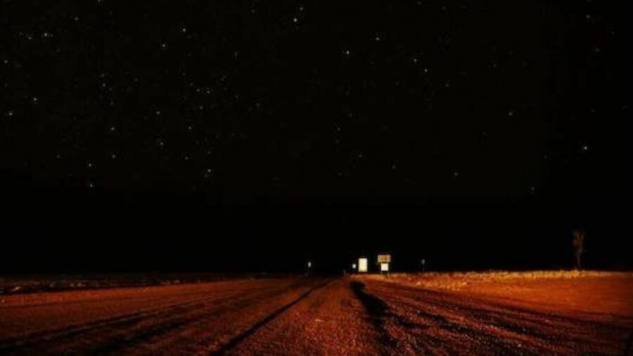 A black night sky is contrasted with the bright red dirt road. Slightly lit up by the mysterious Min Min Lights. 